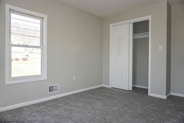 unfurnished bedroom featuring a closet, visible vents, dark carpet, and baseboards