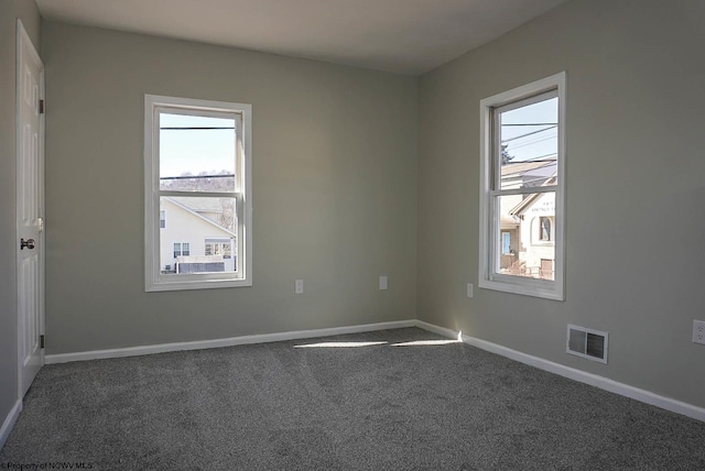 spare room featuring dark colored carpet, visible vents, and baseboards