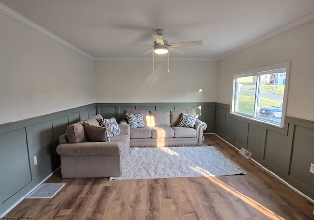 living area featuring visible vents, wood finished floors, a wainscoted wall, and crown molding