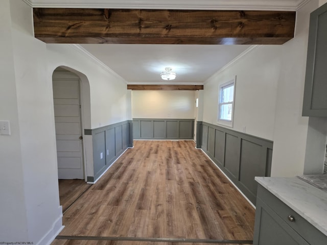 empty room featuring arched walkways, wood finished floors, wainscoting, and crown molding