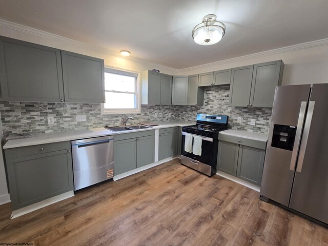 kitchen with gray cabinets, appliances with stainless steel finishes, wood finished floors, and a sink