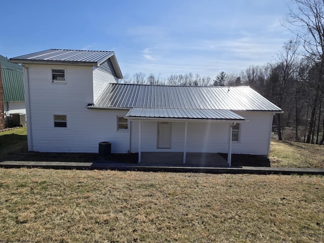 back of property with central air condition unit, a lawn, and metal roof