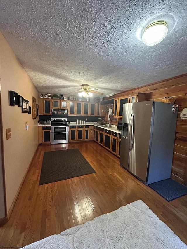 kitchen featuring light countertops, wood finished floors, brown cabinetry, stainless steel appliances, and a sink