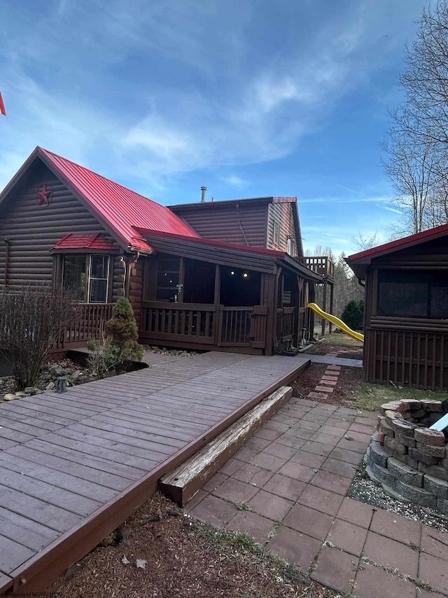 rear view of property with an outdoor fire pit, log veneer siding, metal roof, and a deck