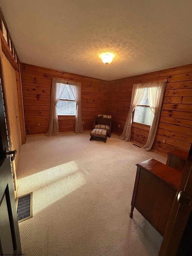 unfurnished room featuring light colored carpet, visible vents, wood walls, and a textured ceiling