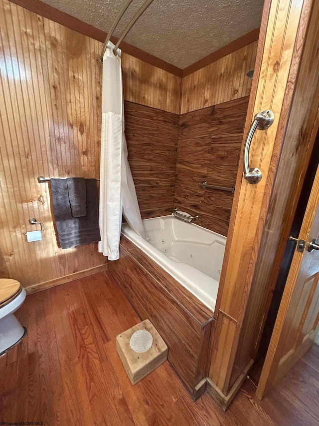 bathroom featuring toilet, a combined bath / shower with jetted tub, a textured ceiling, wood finished floors, and wood walls