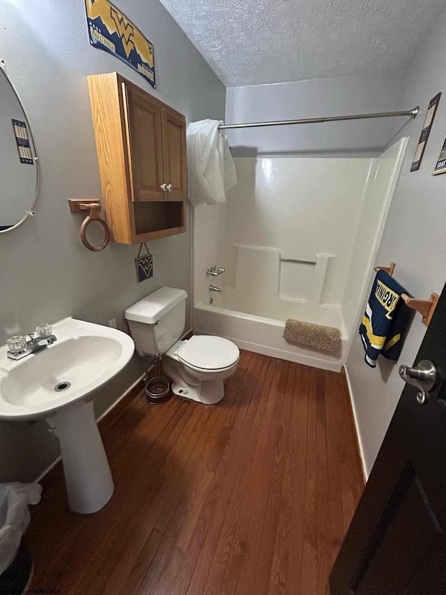 full bath with toilet, shower / bath combination, wood finished floors, a textured ceiling, and a sink