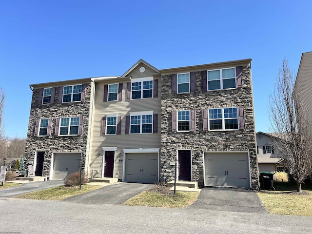 multi unit property featuring a garage, stone siding, and driveway