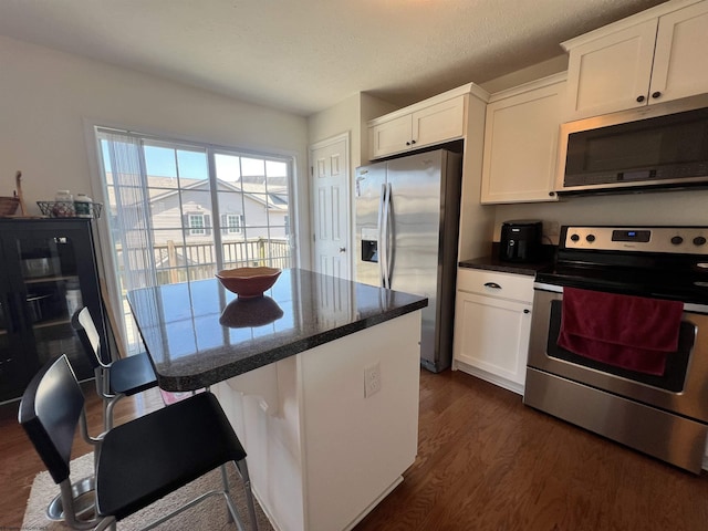 kitchen with a kitchen island, white cabinetry, appliances with stainless steel finishes, a breakfast bar area, and dark wood-style flooring