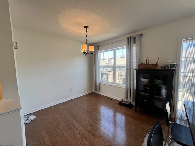 dining area with dark wood-type flooring, baseboards, visible vents, and a chandelier