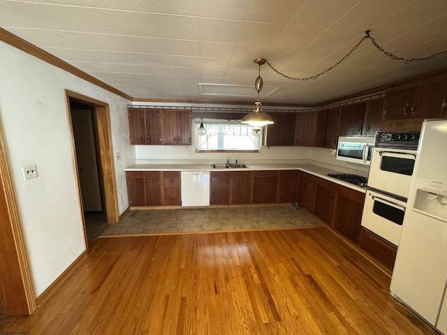 kitchen with light countertops, ornamental molding, wood finished floors, white appliances, and a sink