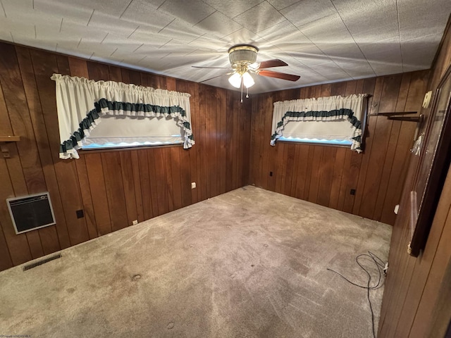 spare room with carpet, visible vents, wood walls, and ceiling fan