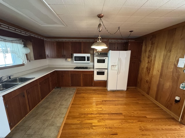 kitchen featuring white appliances, light wood-style flooring, a sink, hanging light fixtures, and light countertops