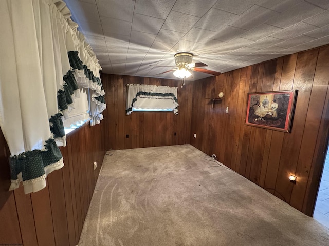 carpeted spare room featuring wooden walls and a ceiling fan