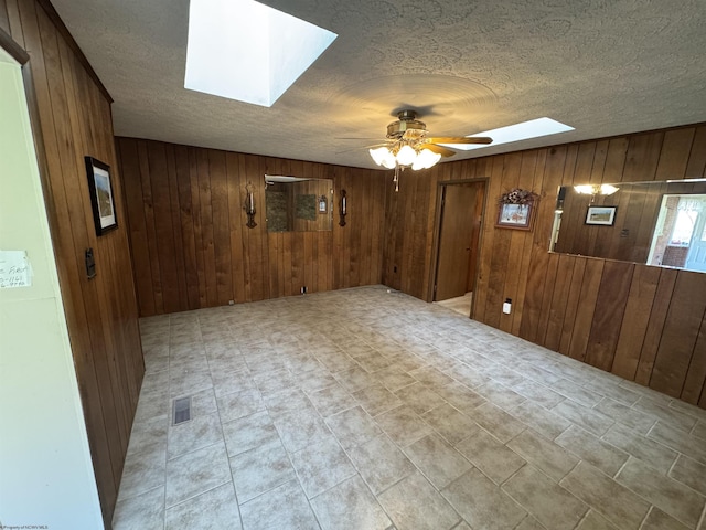 spare room with wooden walls, visible vents, a skylight, and a ceiling fan