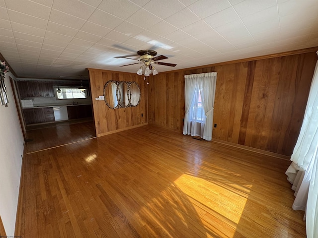 unfurnished living room featuring wooden walls, a ceiling fan, and wood finished floors