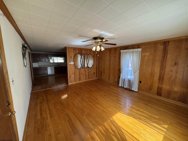 unfurnished living room featuring a healthy amount of sunlight, a ceiling fan, wood walls, and wood finished floors