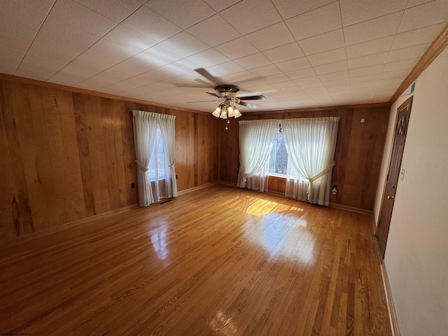 spare room with crown molding, wooden walls, and wood finished floors