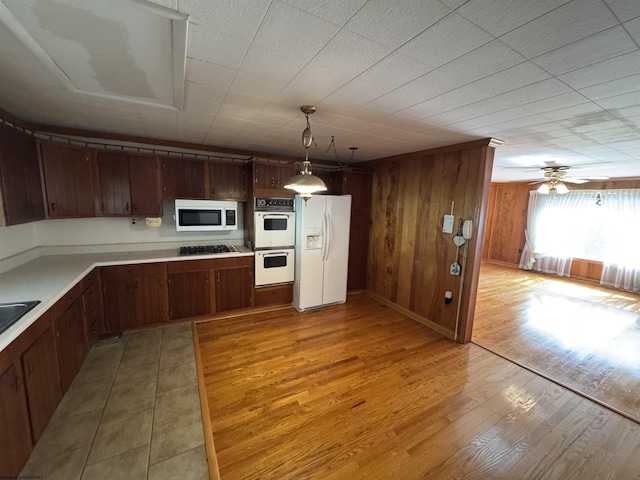 kitchen featuring light wood-type flooring, decorative light fixtures, white appliances, wood walls, and light countertops