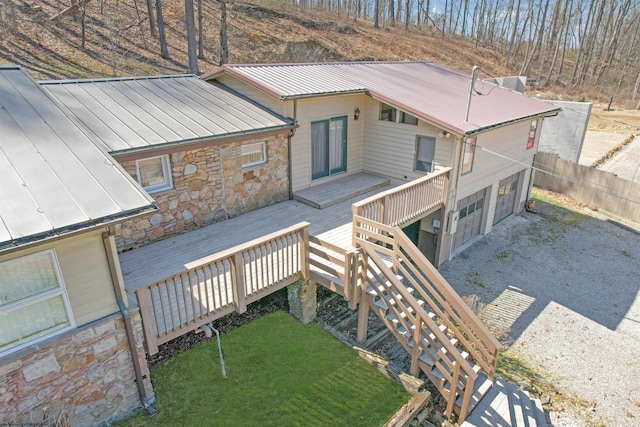 back of house with fence, driveway, a garage, stone siding, and a deck