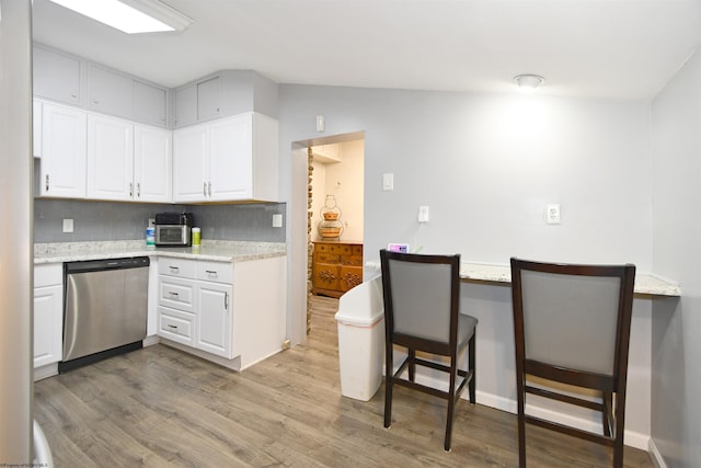 kitchen with wood finished floors, white cabinetry, a kitchen bar, dishwasher, and backsplash