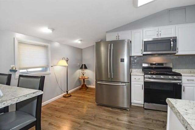 kitchen with lofted ceiling, light countertops, appliances with stainless steel finishes, white cabinetry, and backsplash