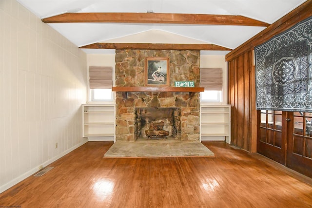 living room with visible vents, a stone fireplace, lofted ceiling with beams, and wood finished floors