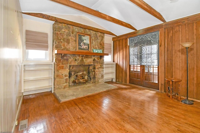 unfurnished living room with wood finished floors, visible vents, vaulted ceiling with beams, french doors, and wood walls