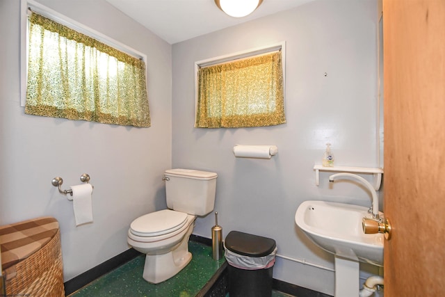 half bath featuring toilet, baseboards, and a sink