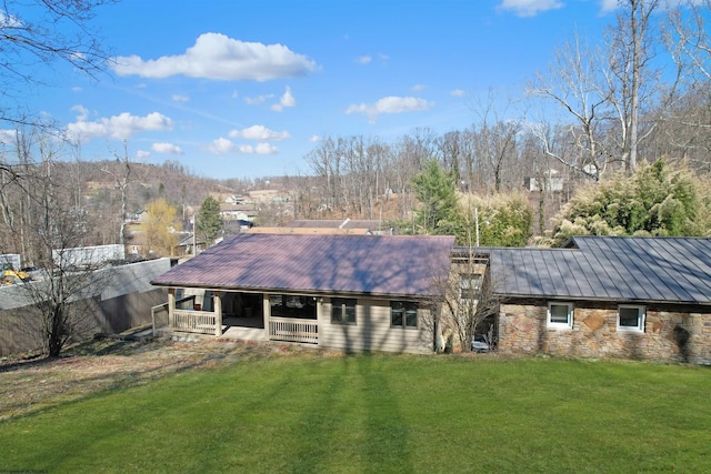 back of house with stone siding, a lawn, and metal roof