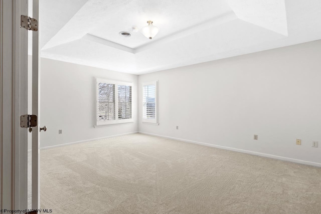 carpeted empty room featuring a tray ceiling, visible vents, and baseboards