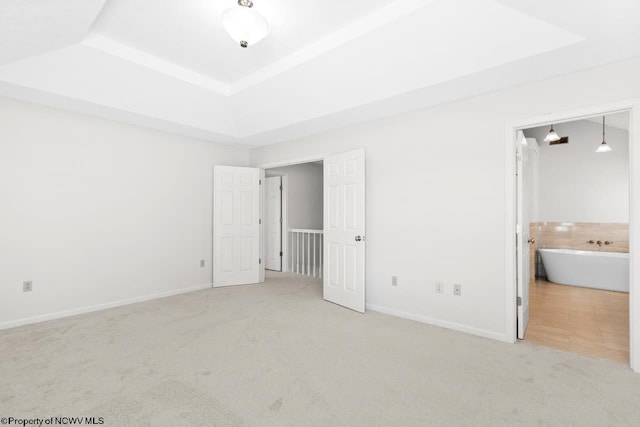 unfurnished bedroom with a raised ceiling, carpet, baseboards, and ensuite bathroom