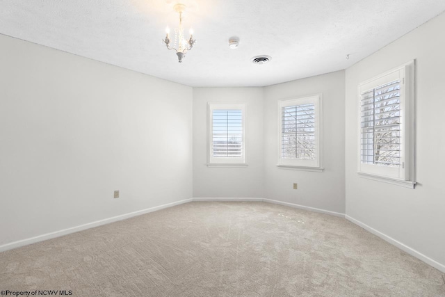 unfurnished room featuring visible vents, a notable chandelier, a textured ceiling, carpet flooring, and baseboards