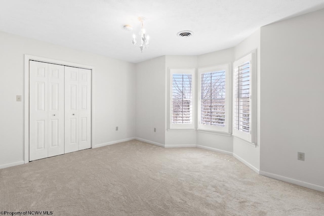 unfurnished bedroom featuring carpet flooring, visible vents, an inviting chandelier, and baseboards