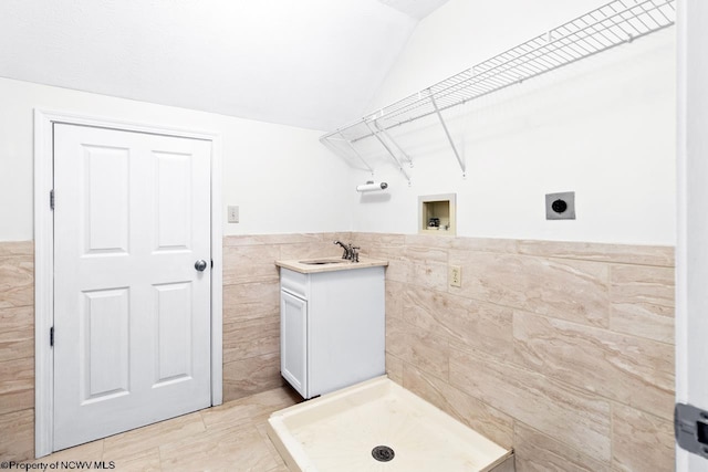 bathroom featuring a stall shower, a sink, tile walls, wainscoting, and lofted ceiling