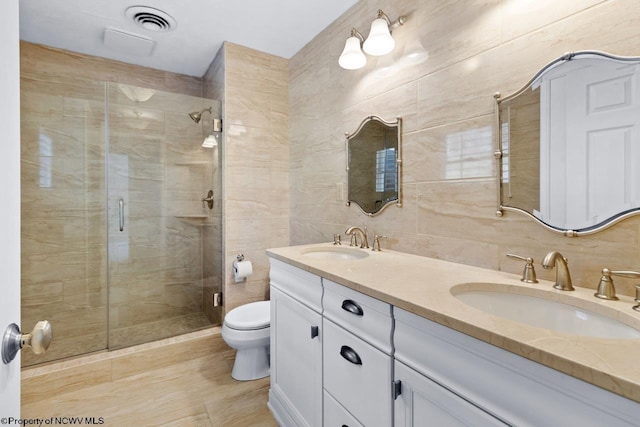 bathroom featuring tile walls, toilet, a stall shower, and a sink