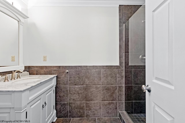 bathroom with tile walls, tiled shower, vanity, and crown molding