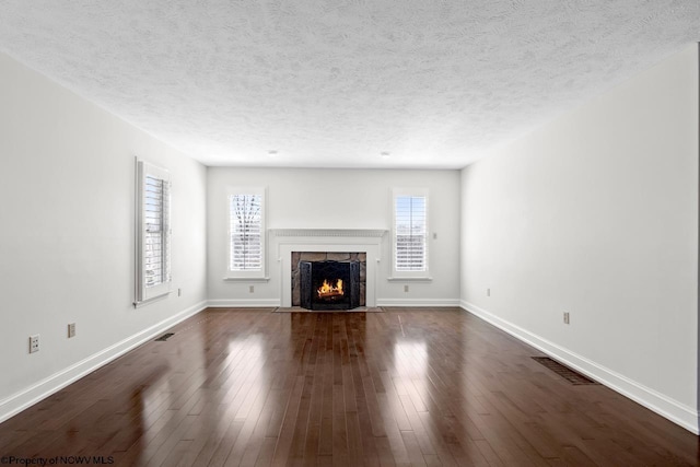 unfurnished living room featuring baseboards, visible vents, a premium fireplace, dark wood finished floors, and a textured ceiling