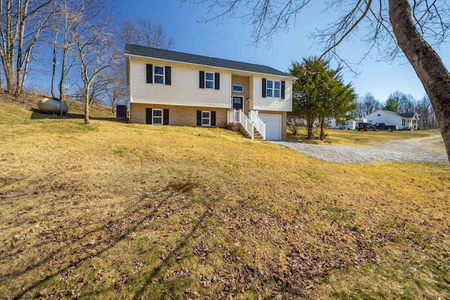 bi-level home with gravel driveway, a front lawn, a garage, and brick siding