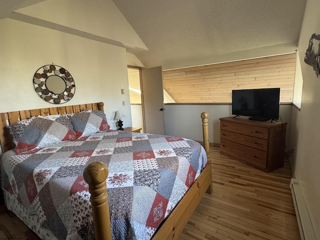 bedroom featuring a baseboard heating unit, lofted ceiling, and hardwood / wood-style floors