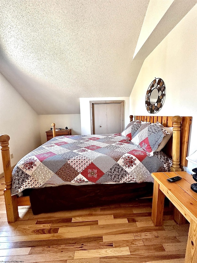 bedroom featuring lofted ceiling, a textured ceiling, and wood finished floors