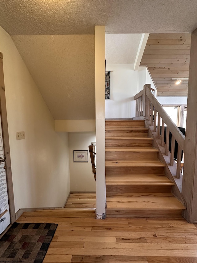 stairs featuring vaulted ceiling, wood-type flooring, and a textured ceiling