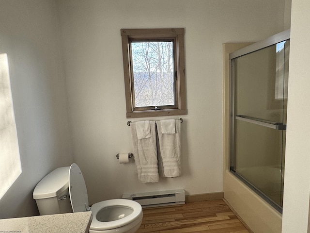 bathroom featuring toilet, wood finished floors, bath / shower combo with glass door, baseboards, and baseboard heating