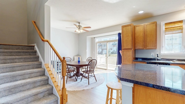 kitchen with dark stone countertops, a breakfast bar, recessed lighting, ceiling fan, and light wood-style floors