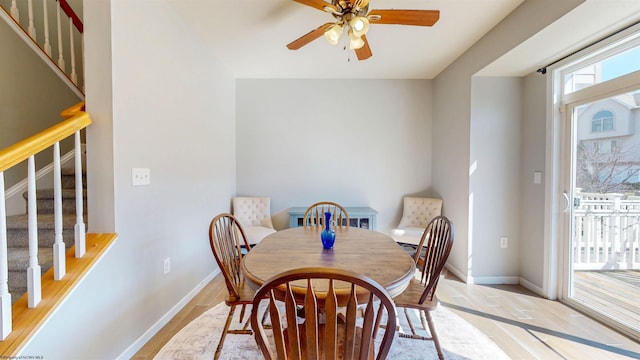 dining space with stairway, light wood-style flooring, a ceiling fan, and baseboards