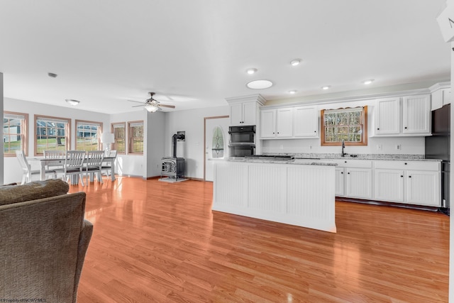 kitchen featuring light wood finished floors, a sink, black appliances, white cabinets, and open floor plan