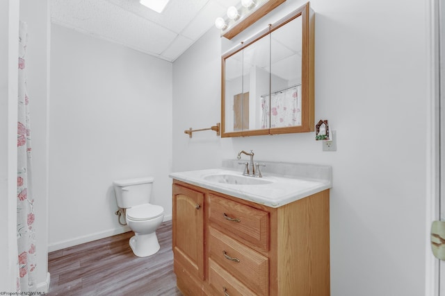 full bathroom featuring toilet, a drop ceiling, wood finished floors, baseboards, and vanity