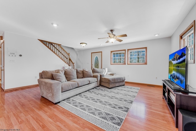 living area featuring baseboards, a ceiling fan, stairs, and light wood finished floors