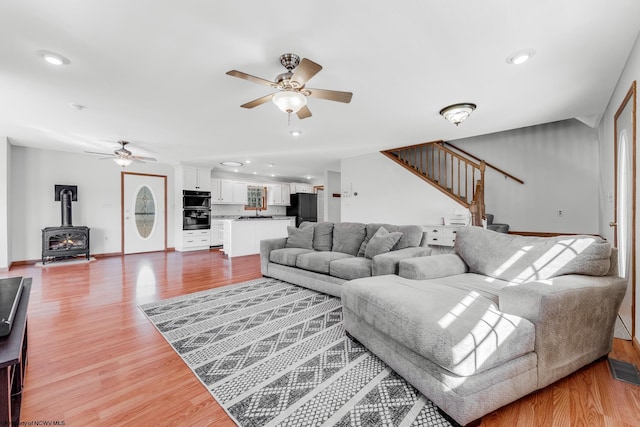 living area with stairway, a ceiling fan, wood finished floors, and a wood stove