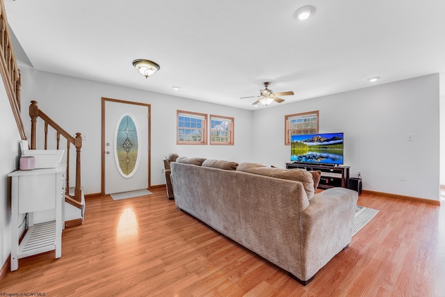 living room with stairway, baseboards, light wood-style floors, and a ceiling fan